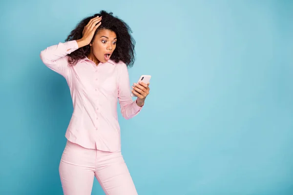 電話を保持している驚くべき波状の暗い肌の女性の写真悪いニュースを読んで口を開けて否定的なコメントはピンクのシャツパンツ隔離された青の色の背景を着用 — ストック写真