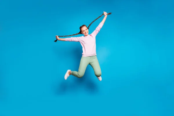 Foto de longitud completa de positivo alegre niña millennial saltar mantenga sus trenzas tienen diversión desgaste casual estilo traje blanco zapatillas aisladas sobre fondo de color azul —  Fotos de Stock