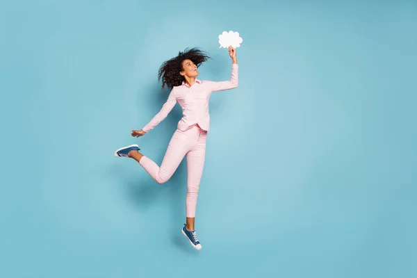 Foto de cuerpo completo de la señora de piel bastante oscura saltando alto sosteniendo la mente de la nube de papel en la mano forma creativa de comunicación desgaste pantalones de camisa rosa aislado fondo de color azul —  Fotos de Stock