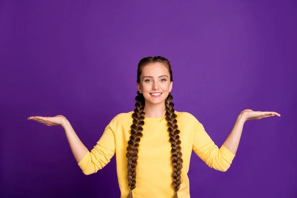 Zdjęcie niesamowite menedżer pani długie warkocze doradztwo chłodne ceny zakupów gospodarstwa dwa nowe produkty na otwarte ramiona nosić casual żółty pullover odizolowany fioletowy kolor tła — Zdjęcie stockowe
