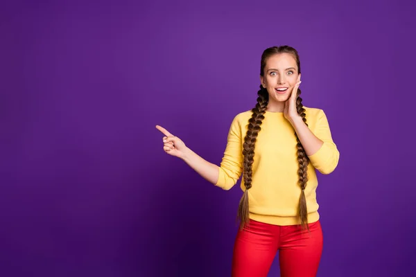 Фото красивих леді довгі коси, що вказують на порожній простір палець, що радить прохолодно низькі ціни на покупки носити повсякденний жовтий пуловер червоних штанів ізольований фіолетовий кольоровий фон — стокове фото