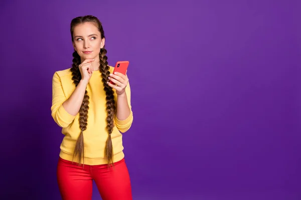 Foto de increíble adolescente dama sosteniendo teléfono buscando espacio vacío tienen pensamiento creativo para el nuevo post desgaste casual amarillo jersey rojo pantalones aislados color púrpura fondo —  Fotos de Stock