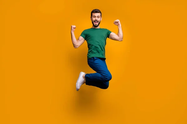Volledige lengte foto van vrolijke gekke funky guy jump win loterij tonen zijn kracht biceps triceps raise vuisten schreeuwen ja dragen groen t-shirt geïsoleerd over gele kleur achtergrond — Stockfoto