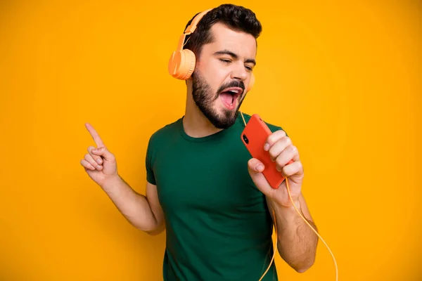 Joven chico alegre venenoso escuchar música estéreo de auriculares naranjas como la música utilizar el teléfono celular como micrófono imaginar que fresco artista estrella de rock usar traje elegante aislado color amarillo fondo — Foto de Stock
