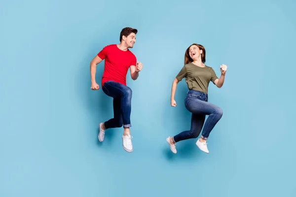 Volledige foto van charmante echtgenoten ontspannen rust springen run dragen groen rood t-shirt denim jeans sneakers geïsoleerd over blauwe kleur achtergrond — Stockfoto