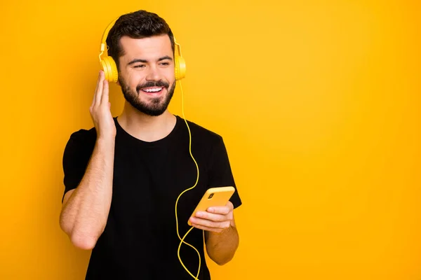 Portret van positieve vrolijke jongen hebben lente weekend luisteren muziek gebruik moderne headset van zijn smartphone dragen goed uitziende geïsoleerd over gele kleur achtergrond — Stockfoto