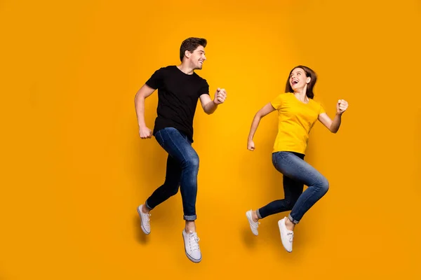 Πλήρης φωτογραφία μεγέθους του αθλητικού άντρα και γυναίκα ζευγάρι άλμα υψηλής δραστήριος τρόπος ζωής ζευγάρι μαραθώνιους συμμετέχοντες φορούν casual τζιν μαύρο t-shirts απομονωμένο κίτρινο φόντο χρώμα — Φωτογραφία Αρχείου