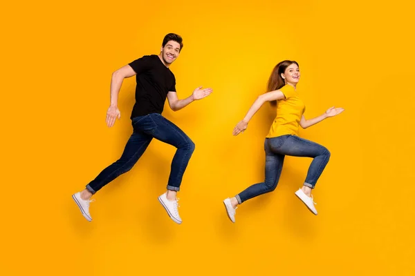 Full body foto van cool guy dame paar springen hoog actieve manier van leven joggen elke ochtend voor te bereiden paar race dragen casual jeans zwart t-shirts geïsoleerde gele kleur achtergrond — Stockfoto