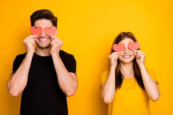 Photo of cheerful cute nice charming pretty sweet couple hiding their eyes behind small posctards heart smiling toothily isolated vivid yellow color background — Stock Photo, Image