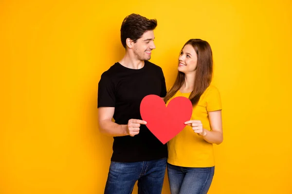 Φωτογραφία του χαρούμενα γοητευτικό διασκέδαση funky χαριτωμένο γλυκό όμορφη κοιτάζοντας ο ένας τον άλλο κρατώντας μεγάλη κόκκινη καρδιά της αγάπης χαμογελώντας οδοντικά σε μαύρο τζιν t-shirt που απομονώνονται σε φωτεινό λαμπερό χρώμα φόντο — Φωτογραφία Αρχείου