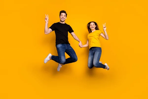 Full body photo of crazy guy lady couple jumping high holding arms showing v-sign symbols saying hi wear casual jeans noir t-shirts isolé couleur jaune fond — Photo