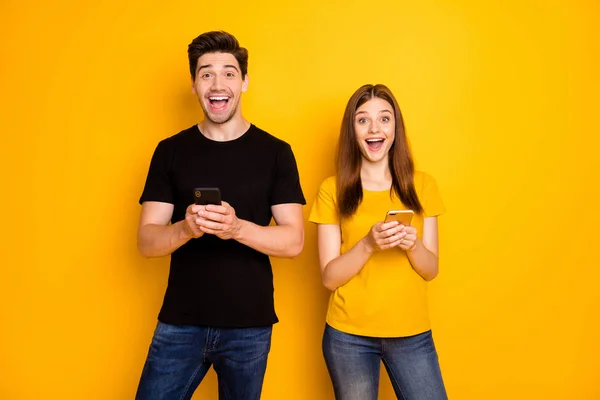 Foto de elegante alegre positivo lindo divertido divertido agradable encantadora bonita pareja con pantalones vaqueros camiseta negra denim haber comprado nuevos teléfonos con ventas aislado color vivo fondo —  Fotos de Stock