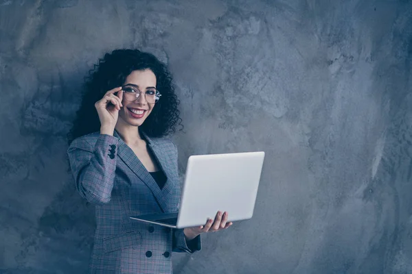 Portrait of her she nice attractive lovely cheerful cheery confident smart clever wavy-haired girl holding in hands laptop touching specs isolated over gray concrete wall background — Stock Photo, Image