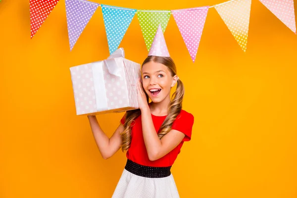 Photo of pretty funny little lady long tails hairstyle birthday party event hold big giftbox guessing what inside box wear paper hat casual red white dress isolated yellow color background