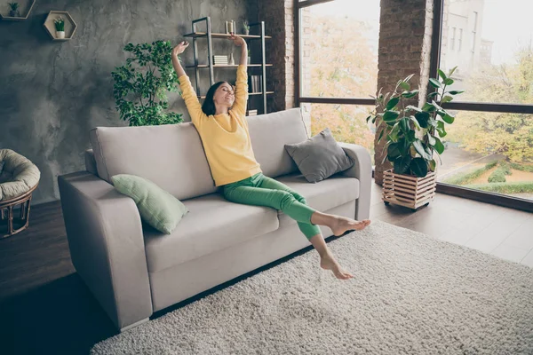 Foto de tamaño completo de niña positiva sentarse diván después del sueño suave estirar sus manos se sienten contentos en el apartamento de la casa en el interior — Foto de Stock