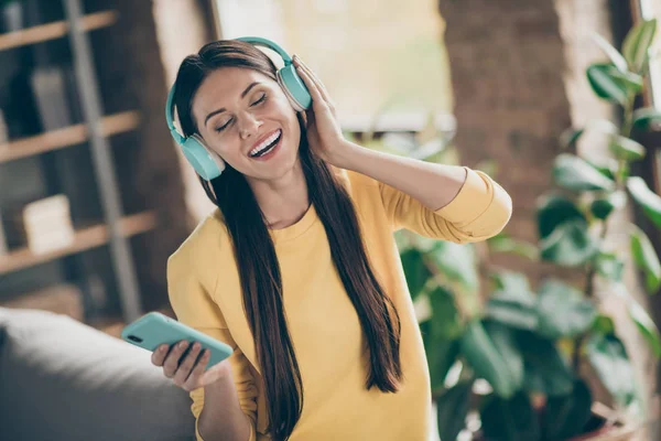 Retrato de chica alegre positiva escuchar música en su teléfono inteligente elegir melodía disfrutar de la canción usar suéter amarillo en el apartamento de la habitación — Foto de Stock