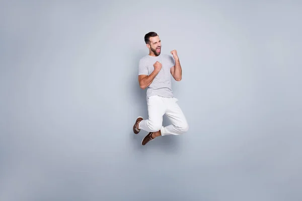 Full length body size view of his he nice attractive fit muscular sporcular cheerful cheery glad bearded guy jumping rejoicing having fun isolated over light grey pastel color background — стоковое фото