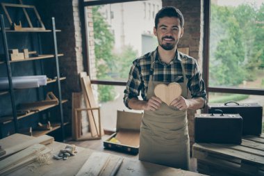 Photo of cheerful positive attractive man holding wooden heart made by himself demonstrating his joinery talent clipart