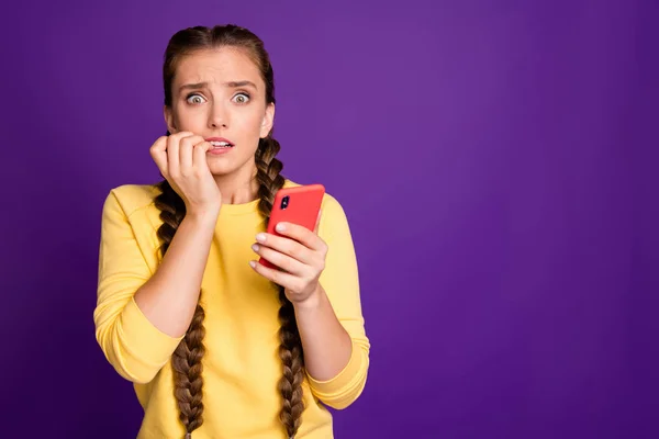 Oh, no. Foto de la señora milenaria sosteniendo lectura de teléfono noticias falsas comentarios ojos llenos de miedo morder los dedos usan suéter amarillo casual aislado color púrpura fondo — Foto de Stock