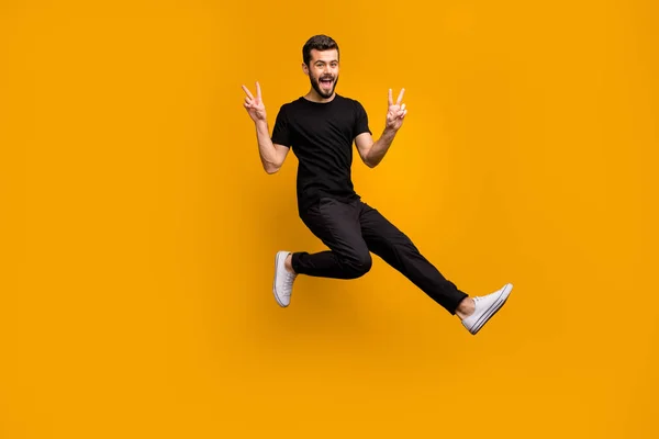 Pełna długość zdjęcie przystojny podekscytowany facet skacze wysokie podnoszące ręce pokazując v-symbole powitanie przyjaciele spotkać ulica nosić czarny t-shirt spodnie odizolowany żółty kolor tło — Zdjęcie stockowe