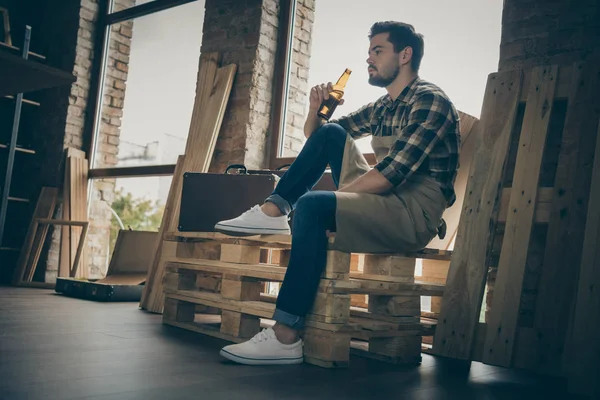 Bajo el ángulo de vista foto del hombre pensativo serio sosteniendo la botella de bebida alcohólica sentado en bloques de madera mirando soñadoramente — Foto de Stock