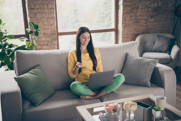 Full length photo of positive cheerful girl sit divan cross legs use computer video call her friends in house indoors — Stock Photo, Image