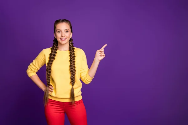 Fénykép a vicces hölgy hosszú fonat frizura jelzi ujj üres tér tanácsadás hűvös vásárlási árak viselése alkalmi sárga pulóver piros nadrág elszigetelt lila színű háttér — Stock Fotó