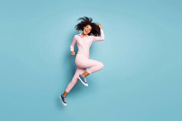 Teljes test profil fotó bájos sötét bőr göndör hölgy jumping magas ünneplő nagy győzelem bajnok viselni rózsaszín ing nadrág cipő elszigetelt kék háttér — Stock Fotó