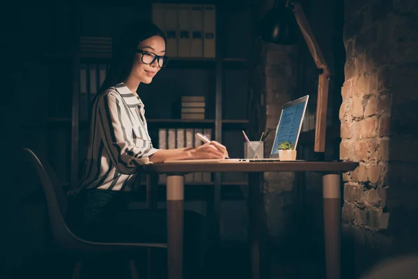 Alacsony látószögű kép ázsiai üzleti hölgy keményen dolgozó személy notebook asztal írás startup ötlet notepad ülés szék formalwear csíkos ing éjszaka sötét modern iroda — Stock Fotó