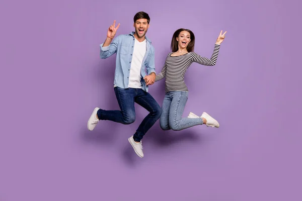 Full length photo of two people couple funny guy lady jumping high holding hands showing v-sign symbols wear stylish casual ρούχα απομονωμένο παστέλ μωβ χρώμα φόντο — Φωτογραφία Αρχείου