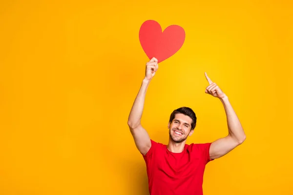 Ritratto di ragazzo allegro positivo tenere carta di carta rossa cuore indice dito presente la sua fidanzata regalo 14-febbraio data indossare abbigliamento stile casual isolato colore brillante sfondo — Foto Stock