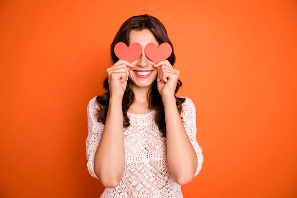 Retrato de menina alegre positivo segurar vermelho pequeno cartão de papel coração esconder seus olhos jogar com o namorado em 14-fevereiro data desgaste boa aparência roupa isolada sobre cor laranja fundo — Fotografia de Stock