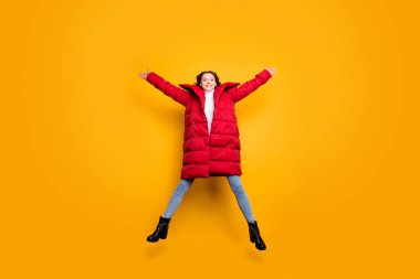 Full length photo of pretty lady jumping high spread hands star shape best weekend wear jeans shoes white pullover red long winter coat isolated yellow color background clipart