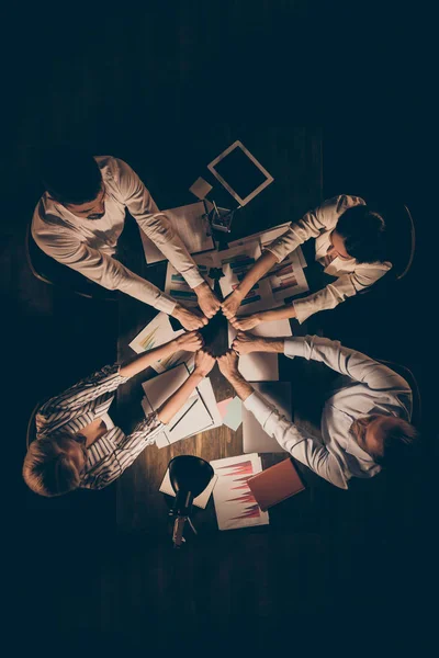 Ângulo alto acima ver foto vertical de quatro pessoas colegas de negócios sentado mesa trabalhando tarde da noite segurando pilha pilha união uma equipe formalwear lâmpada luz dentro de casa — Fotografia de Stock