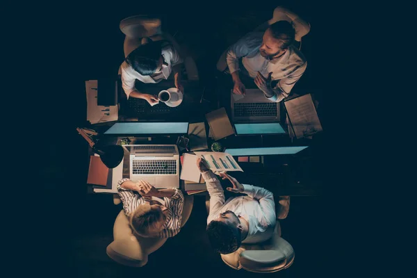 High angle above view photo of hard-working four business people working overtime drinking coffee chat friendly little break lamp light dark office in doors — Zdjęcie stockowe