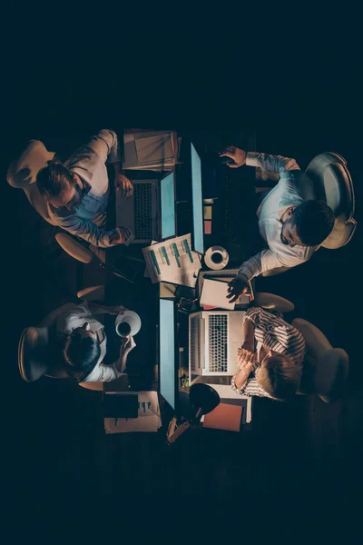 Вертикальный сверху под высоким углом зрения четырех трудолюбивых умных бизнесменов ИТ-гик опытных квалифицированных менеджеров, создающих веб-дизайн заказ клиента на поздней ночью на рабочем месте станции — стоковое фото