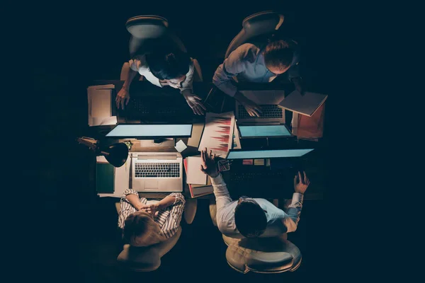 High angle above view photo of hard-working four busy business men women working overtime looking computer screen talking about startup lamp light dark office in doors — Zdjęcie stockowe