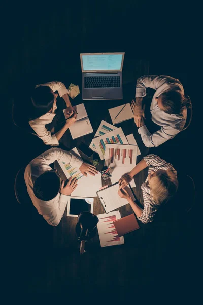 Ângulo alto acima ver foto vertical de quatro parceiros homens de negócios mulheres que trabalham horas extras discutir nova startup olhando lâmpada notebook escritório escuro luz dentro de casa — Fotografia de Stock