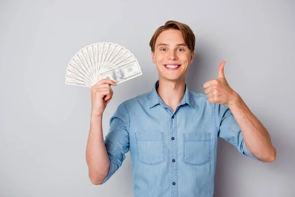 Portret van positieve content guy krijgen miljoen dollar houden geld fan credit bank genieten van winst show duim omhoog raden advertenties dragen trendy outfit geïsoleerd over grijze kleur achtergrond — Stockfoto