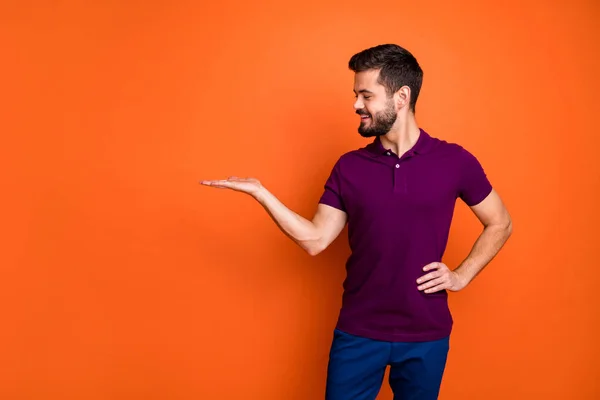 Foto de alegre homem bonito positivo olhando para o espaço vazio realizada com a mão na cintura em calças azuis isolado fundo de cor vívida — Fotografia de Stock