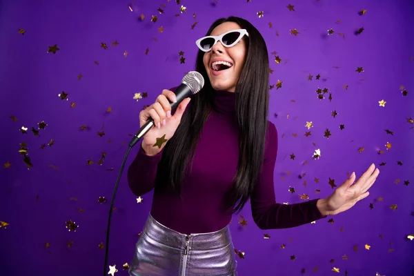 时尚时尚的休闲女友对着话筒唱歌的照片，她在卡拉OK酒吧享受着离群索居的艳丽背景紫色 — 图库照片
