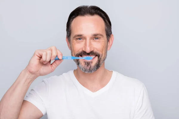 Close-up foto van volwassen man met hand nieuwe tandenborstel schoonmaken tanden verbazingwekkend resultaat goede kwaliteit product slijtage wit t-shirt geïsoleerde grijze kleur achtergrond — Stockfoto