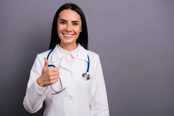 Portret pięknej kobiety pediatra polecam szpital pracuje pokazać kciuk do góry znak sugerują doskonałe leczenie nosić stetoskop biały płaszcz izolowany na szarym tle kolor — Zdjęcie stockowe