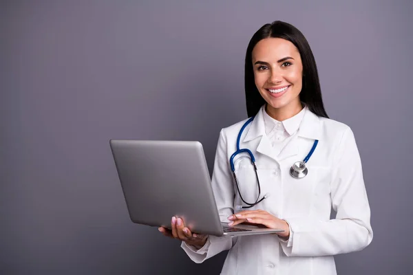 Retrato de mulher bonita experiente médico especialista segurar computador ela usa consultar paciente busca prescrição desgaste casaco branco estetoscópio isolado sobre fundo de cor cinza — Fotografia de Stock