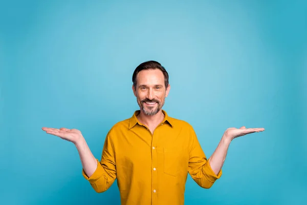 Portret de pozitiv vesel om promoter ține mâinile afișa reduceri de vânzări compara anunțuri promo purta haine stil casual izolate pe fundal de culoare albastră — Fotografie, imagine de stoc