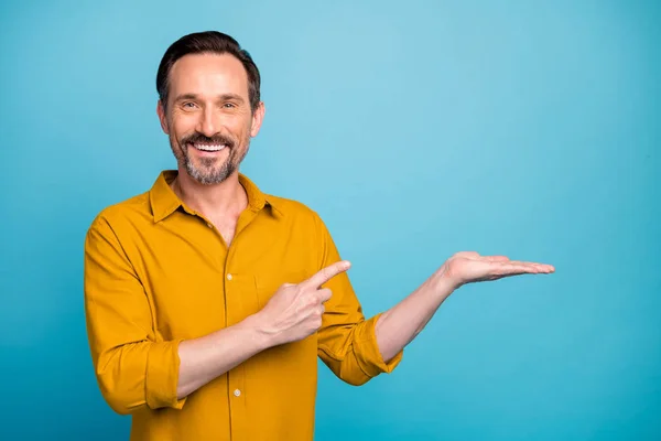 Retrato de positivo homem legal promotor segurar mão presente produto ponto indicador dedo desgaste casual estilo roupas isoladas sobre azul cor fundo — Fotografia de Stock