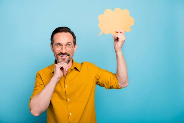 Retrato del hombre de ensueño positivo mantenga el concepto de pensamiento de burbuja de discurso de tarjeta de papel amarillo tiene idea de cómo pasar los fines de semana toque la barbilla desgaste de la mano camisa de estilo casual aislado sobre fondo de color azul — Foto de Stock