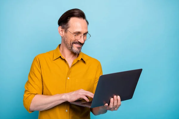 Porträtt av positiv man arbetare arbete på sin dator text med sin familj kollegor bära gul skjorta isolerad över blå färg bakgrund — Stockfoto