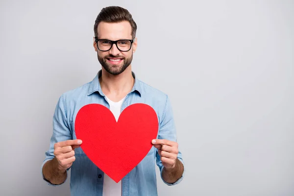 Photo of funny handsome guy holding large red paper heart inviting girlfriend romantic date tender emotions wear specs casual denim clothes isolated grey color background — Stock Photo, Image