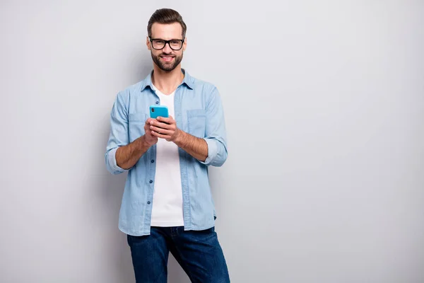 Foto de cara engraçado atraente penteado puro pessoa fácil de ir segurando amigos de bate-papo telefone de navegação usar especificações roupa de ganga casual isolado fundo de cor cinza — Fotografia de Stock